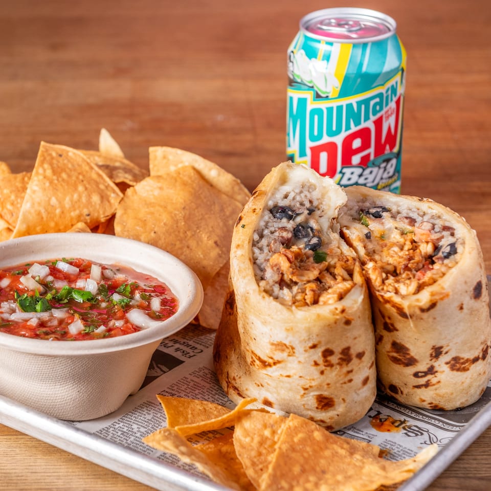 Two burritos, salsa with tortilla chips, and a can of Baja Blast Mountain Dew on a tray.