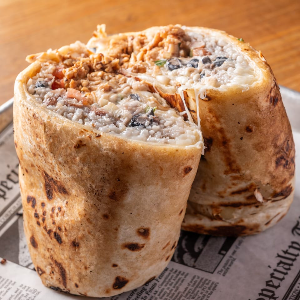 Two large, grilled burritos filled with rice, beans, and meat, served on newspaper.