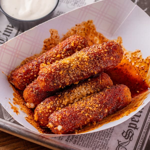 Five crispy, golden-brown mozzarella sticks coated in spices and served in a paper tray with dipping sauce.